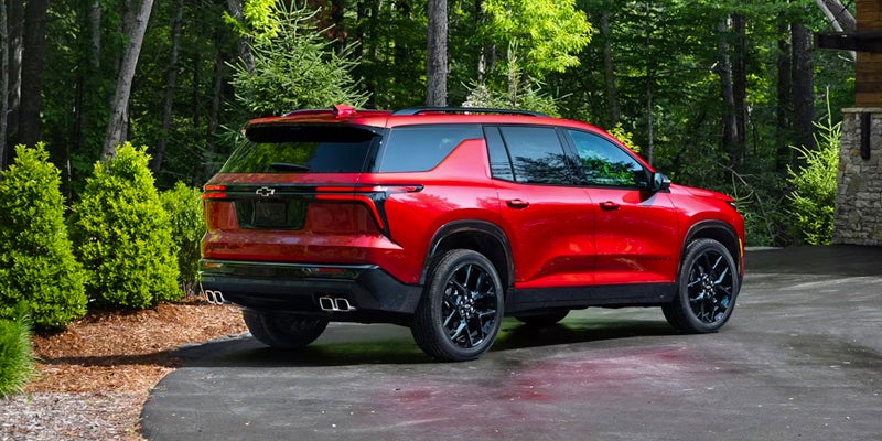 Side profile of a red Chevrolet Traverse parked near trees.