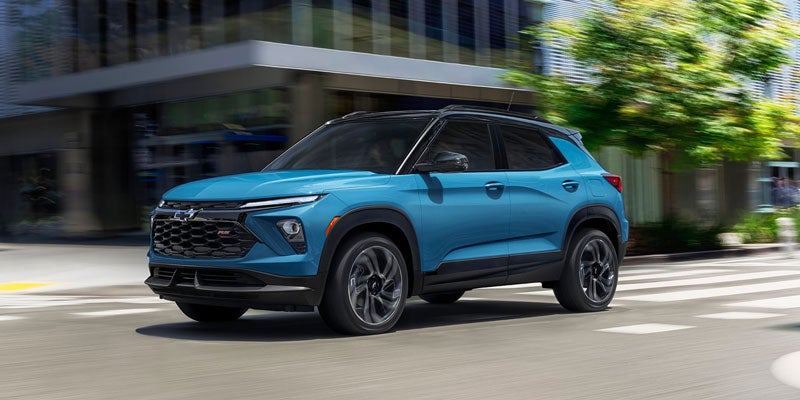 Blue Chevrolet Trailblazer driving on a paved road through trees.