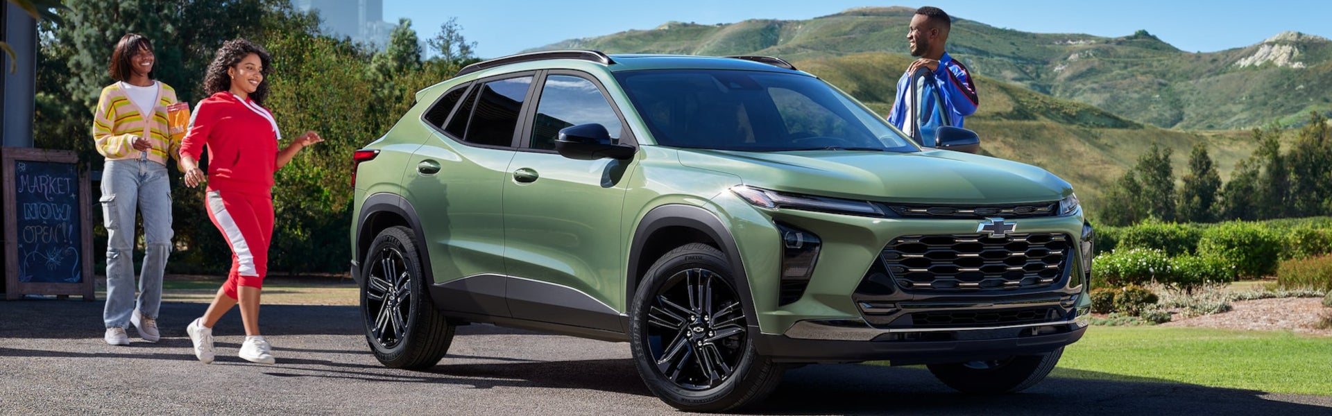 Three people smiling near a green Chevrolet Trax in a sunny park