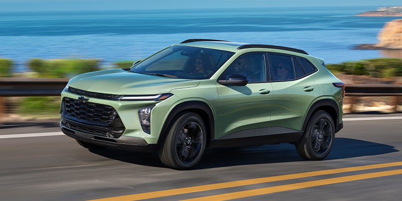 Green Chevrolet Trax driving on a paved road during the day.