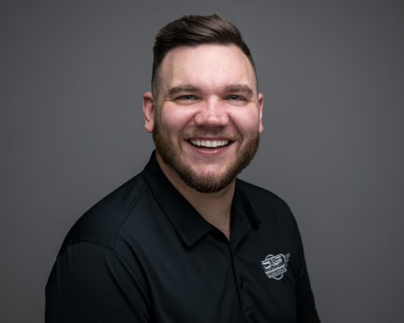Headshot of a smiling man with a short beard and dark hair, wearing a black collared shirt.